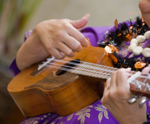 person in purple hawaiian shirt with two lei playing the ukulele
