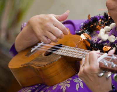 person in purple hawaiian shirt with two lei playing the ukulele