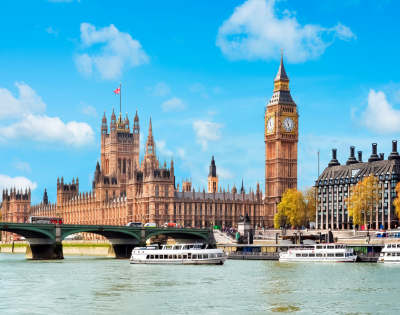 View of the Big Ben and the Houses of Parliament in London across the River Thames with a bridge and boats.