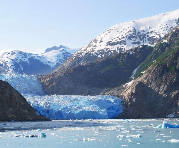 A glacier flowing between mountains into the sea, with icebergs floating in the water.