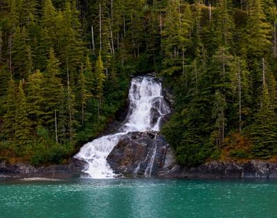A cascading waterfall amidst a forest emptying into a turquoise lake.
