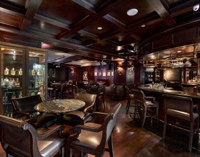 Interior of a moody bar with dark wood burgundy walls and marble tables with a range of spirits in the cabinet