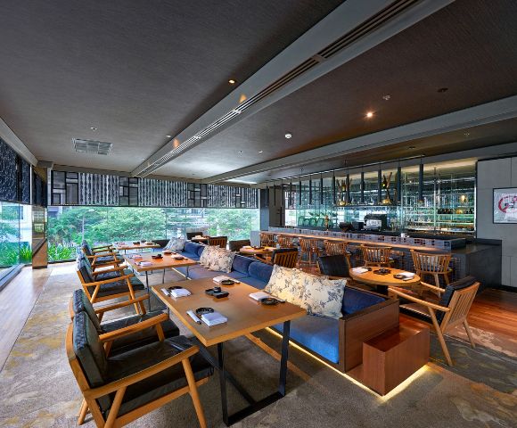 Restaurant seating area with table seating and bar seating and a view into the outside gardens and greenery