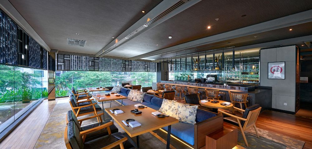 Restaurant seating area with table seating and bar seating and a view into the outside gardens and greenery