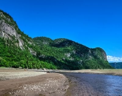 River winding through a sandy shore with forest-covered cliffs under a blue sky.