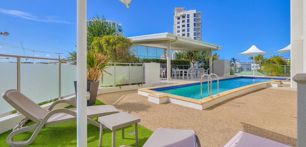 Outdoor pool area with lounge chairs, umbrella, and city buildings in the background at Beach on Sixth Maroochydore in Queensland