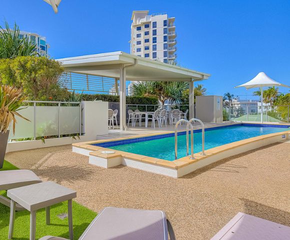 Outdoor pool area with lounge chairs, umbrella, and city buildings in the background at Beach on Sixth Maroochydore in Queensland