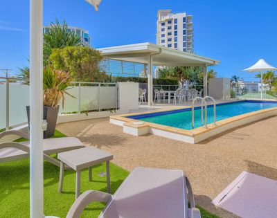 Outdoor pool area with lounge chairs, umbrella, and city buildings in the background at Beach on Sixth Maroochydore in Queensland