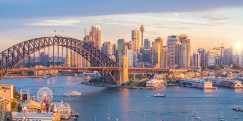 Sunset view of Sydney skyline with the Harbour Bridge and boats on the water.