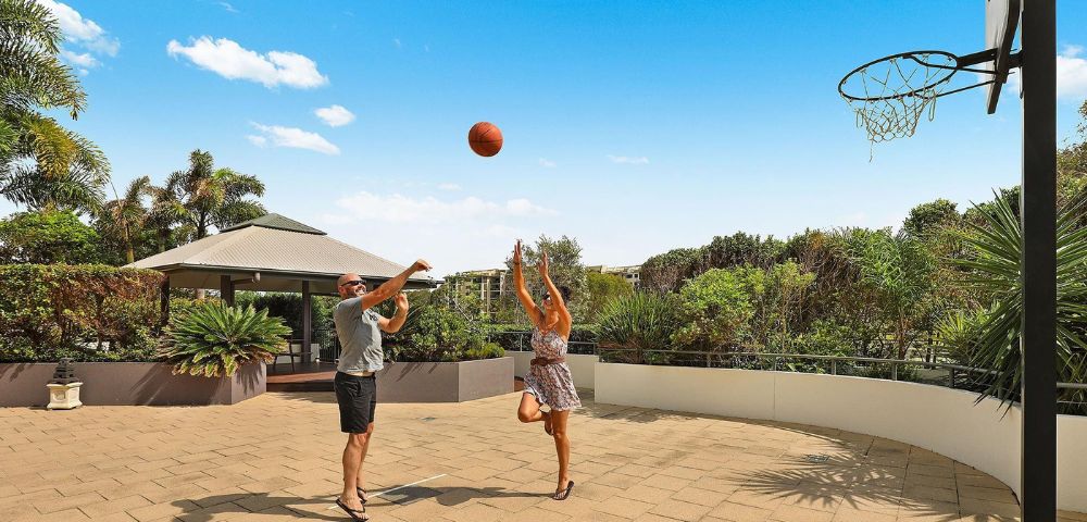 Two people playing basketball on an outdoor court with clear skies.