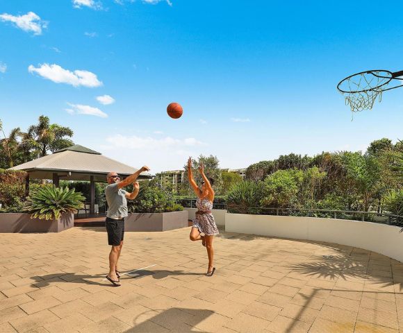 Two people playing basketball on an outdoor court with clear skies.