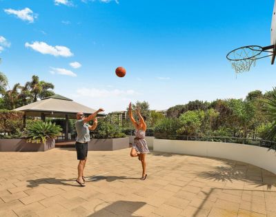 Two people playing basketball on an outdoor court with clear skies.