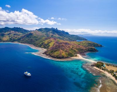 Aerial view of a lush tropical peninsula with clear blue waters and a moored yacht.