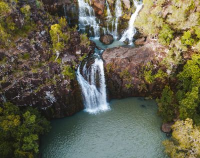 Aerial view of a waterfall cascading into a serene pool surrounded by lush trees.