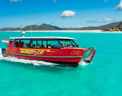 A red speedboat with passengers on turquoise waters near a sandy beach.