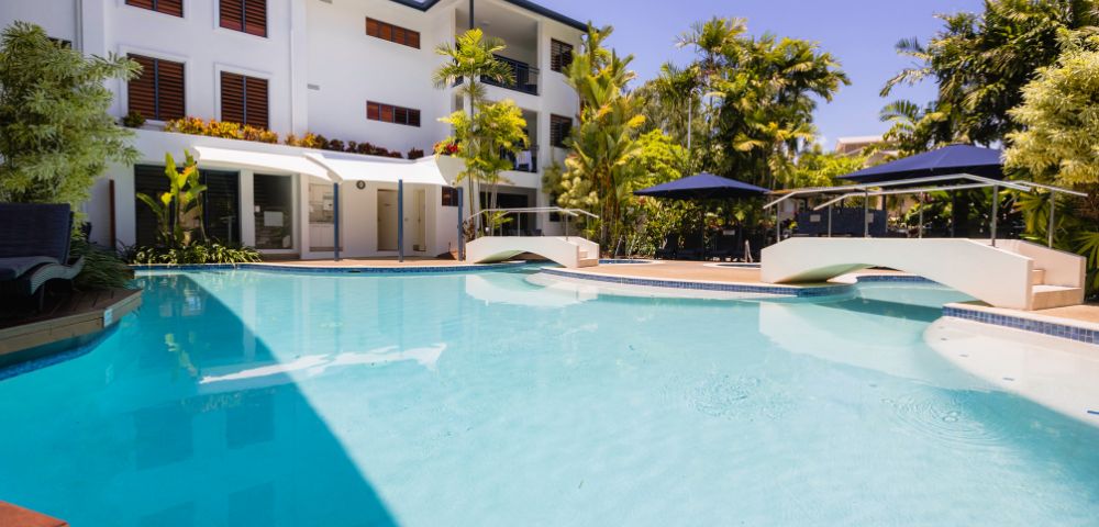 Modern white villa with a swimming pool, sun loungers, and palm trees under a clear blue sky.