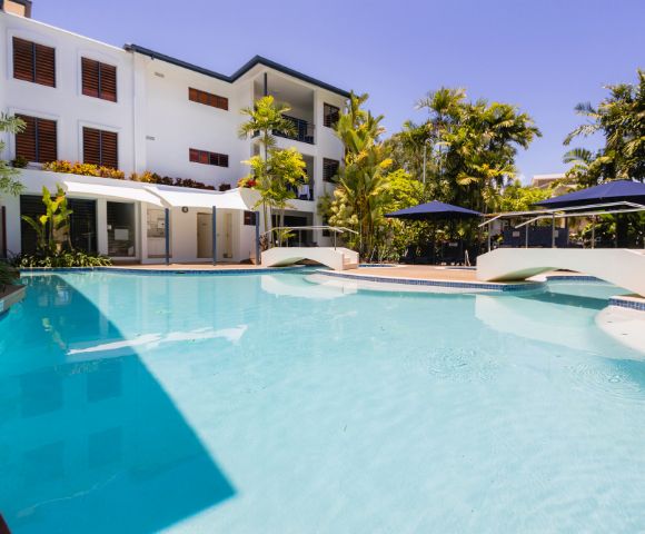 Modern white villa with a swimming pool, sun loungers, and palm trees under a clear blue sky.