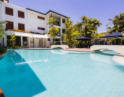 Modern white villa with a swimming pool, sun loungers, and palm trees under a clear blue sky.