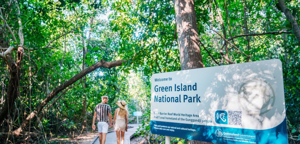 Two people walking into Green Island National Park on a boardwalk beside an informational sign.