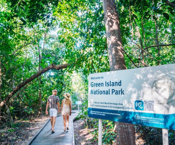 Two people walking into Green Island National Park on a boardwalk beside an informational sign.