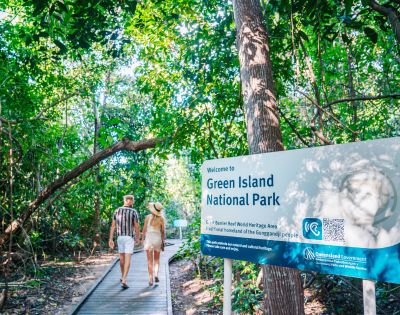Two people walking into Green Island National Park on a boardwalk beside an informational sign.