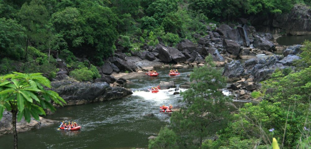Rafting groups navigating through a rocky river surrounded by lush greenery.