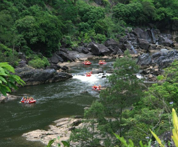 Rafting groups navigating through a rocky river surrounded by lush greenery.