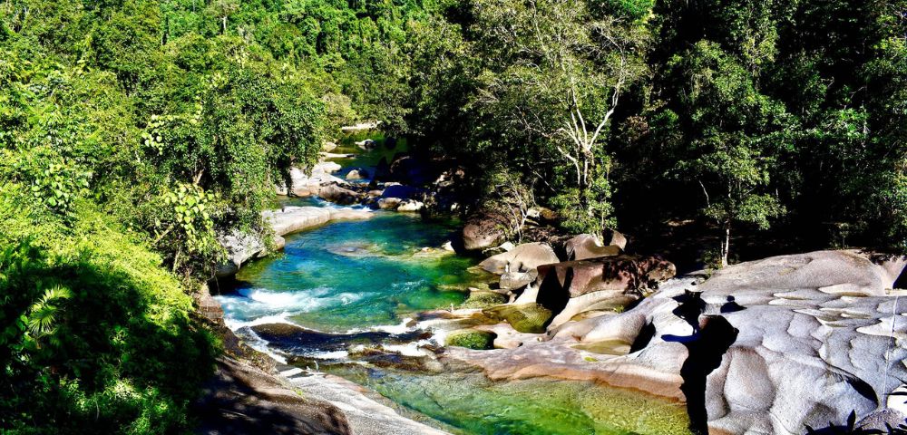 A serene river flowing through a lush forest with clear blue water and smooth rocks.