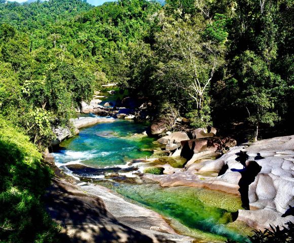 A serene river flowing through a lush forest with clear blue water and smooth rocks.