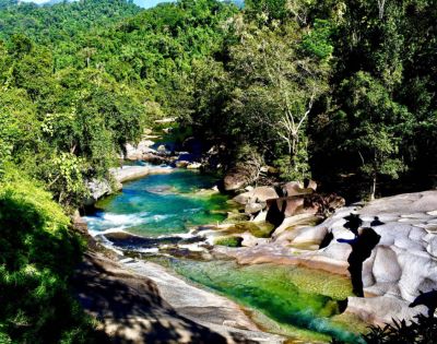 A serene river flowing through a lush forest with clear blue water and smooth rocks.