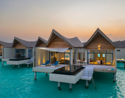 Overwater bungalows with thatched roofs at sunset, extending into a turquoise sea.