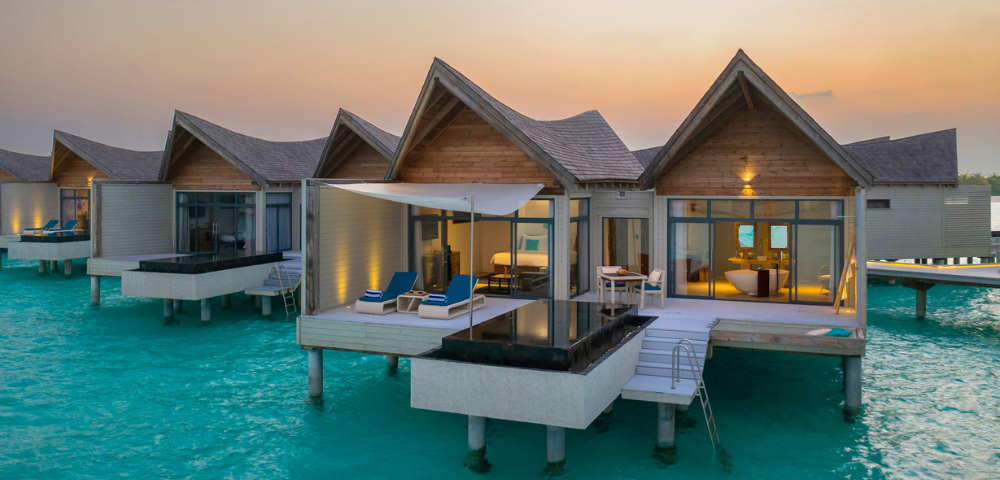 Overwater bungalows with thatched roofs at sunset, extending into a turquoise sea.