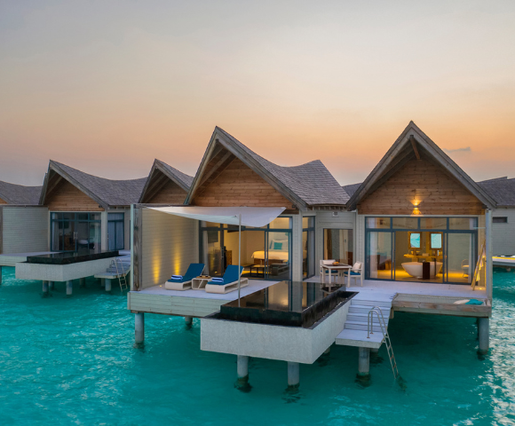 Overwater bungalows with thatched roofs at sunset, extending into a turquoise sea.