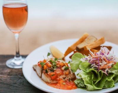 Gourmet fish dish with salad and a glass of rosé wine on a wooden table.