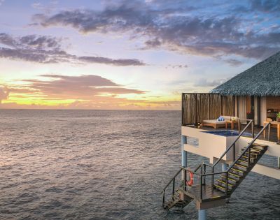 Overwater bungalow with stairs leading into the sea at sunset.