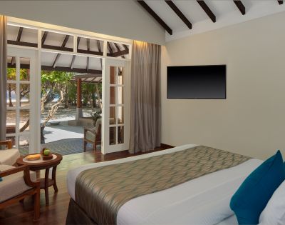 A modern bedroom with an open door to a beach view, a large bed, and a wall-mounted TV.
