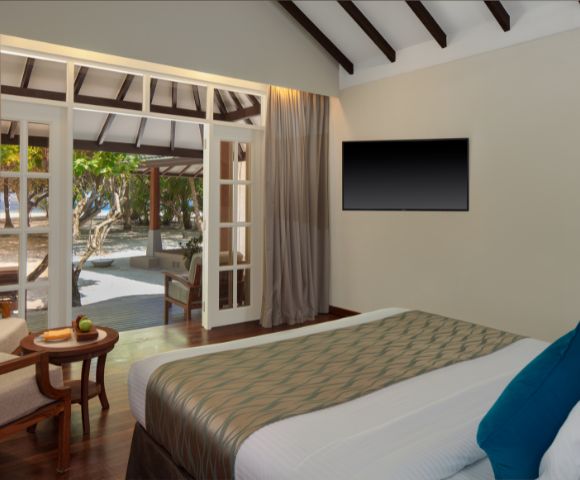 A modern bedroom with an open door to a beach view, a large bed, and a wall-mounted TV.