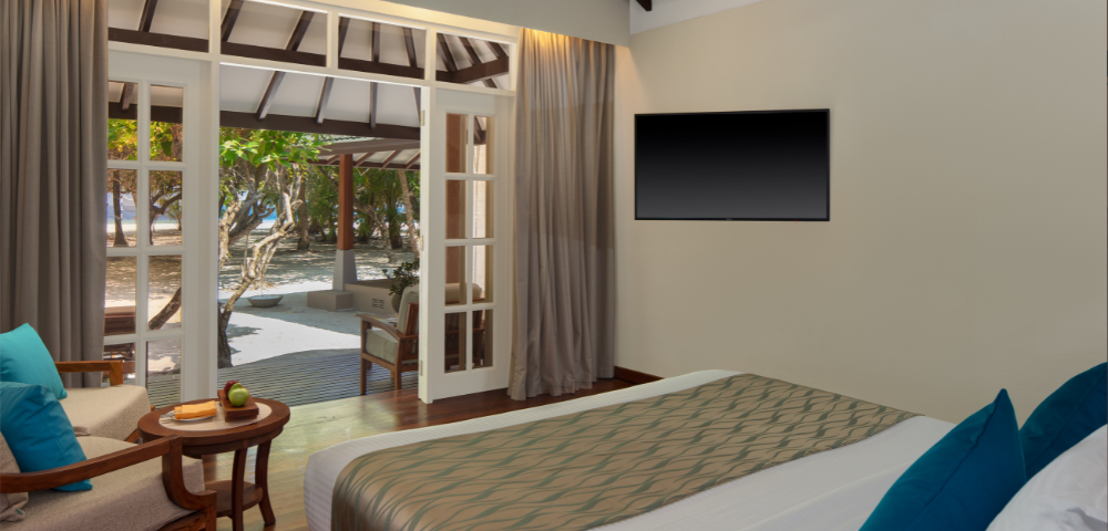 A modern bedroom with an open door to a beach view, a large bed, and a wall-mounted TV.