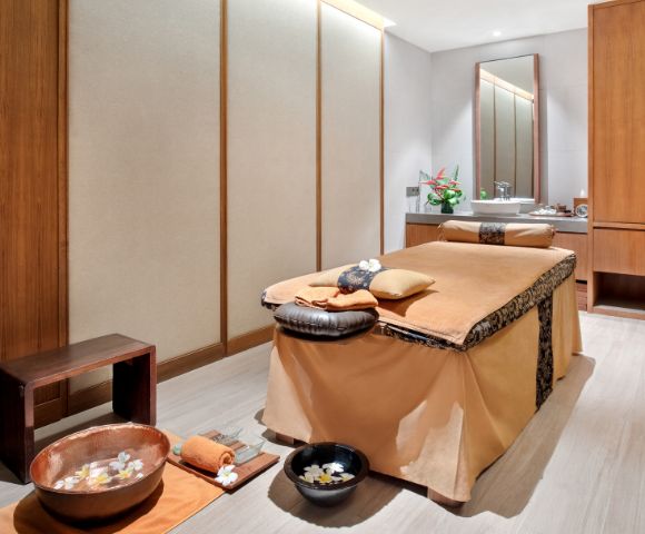 A serene spa room with a massage table, wooden accents, and bowls with flowers.