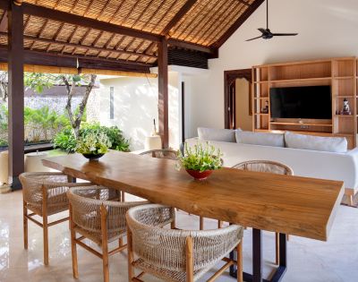 Elegant open living space with a wooden dining table, wicker chairs, and a white sofa under a vaulted ceiling.