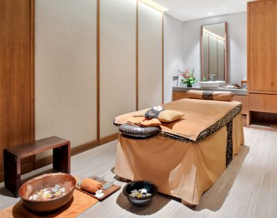 A serene spa room with a massage table, wooden accents, and bowls with flowers.