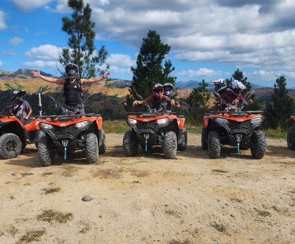 Group of people on ATVs outdoors, with one person celebrating arms outstretched.