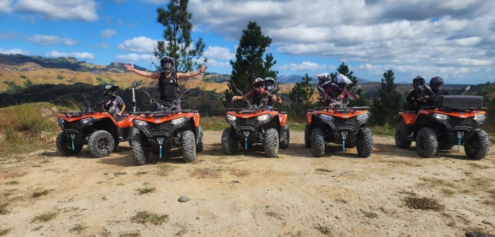 Group of people on ATVs outdoors, with one person celebrating arms outstretched.