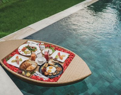 Floating breakfast tray with assorted dishes by a pool.