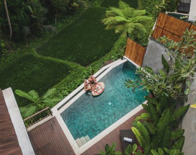 Two people floating on an inflatable in a pool by a lush rice terrace.