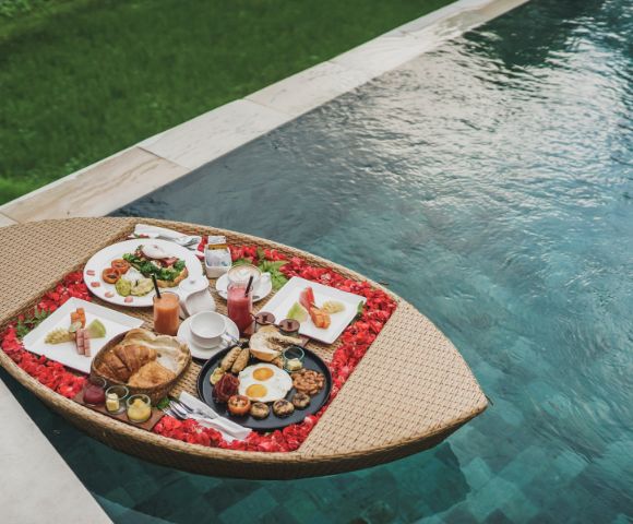 Floating breakfast tray with assorted dishes by a pool.