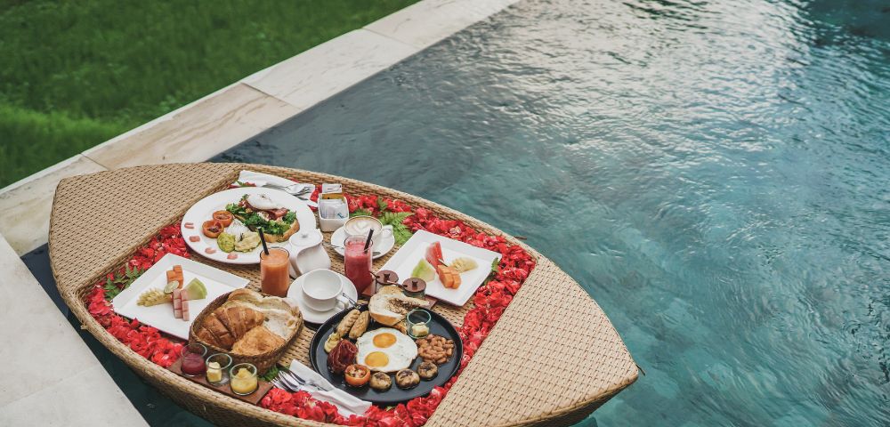 Floating breakfast tray with assorted dishes by a pool.