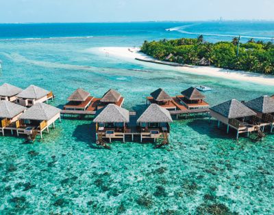 Overwater bungalows with thatched roofs in a clear turquoise sea near a tropical beach.