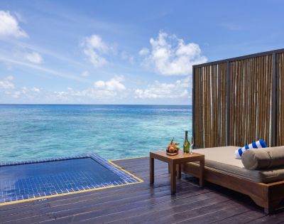 Oceanfront deck with a lounge bed, fruits, wine, and an infinity pool.