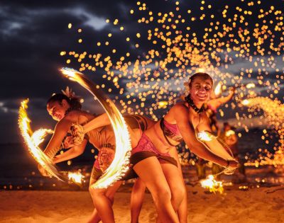 Crowne Plaza Fiji Nadi Bay Resort and Spa Performers twirling fire poi on a beach at night, with sparks flying around.